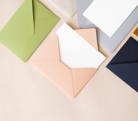 Close-up colorful mail envelopes on beige background flat lay with copy space, top view. Mailing concept isometric. White paper blank mockup for letters, greeting card, postcard, invitation