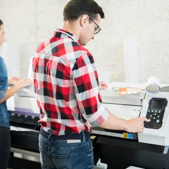 Coworking man and woman in typography office using printing machine while working in team